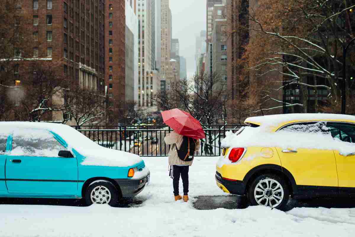 Due auto parcheggiate sotto la neve e una persona con l'ombrello